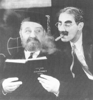 Groucho peers over Robert Greig's shoulder as he reads from a book on anatomy.